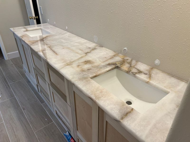 Bathroom vanity with a long marble countertop and two sinks against a tiled floor.