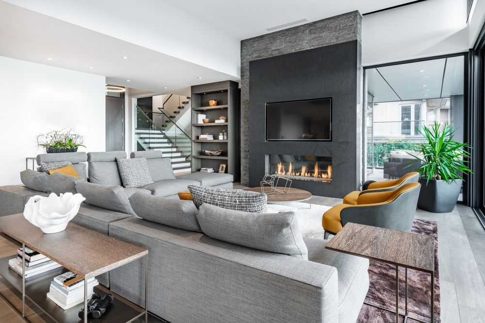 Modern living room with gray sectional, fireplace, built-in shelves, and large mirror wall