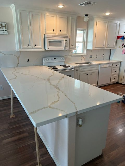 Bright white kitchen with marble island, white cabinets, and dark wood floors