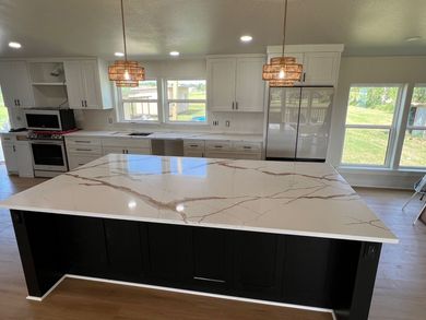 Bright modern kitchen with a large white marble island and black base, stainless appliances, and pendant lights