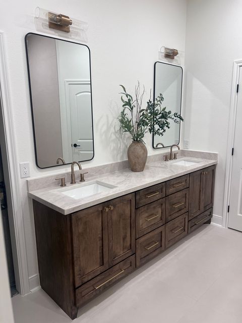 Modern bathroom vanity with double sinks, wood cabinets, mirrors, and a vase of greenery
