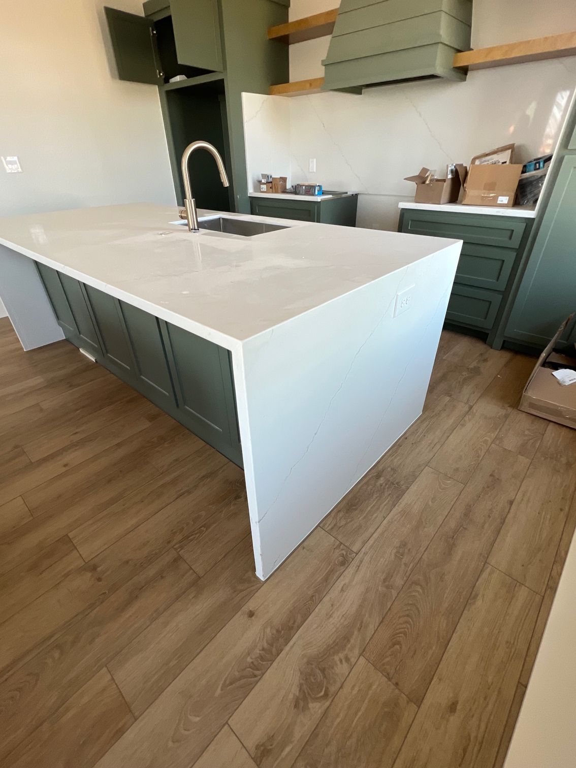 Modern kitchen with a white island, green cabinets, wood floors, and a sink under a black range hood