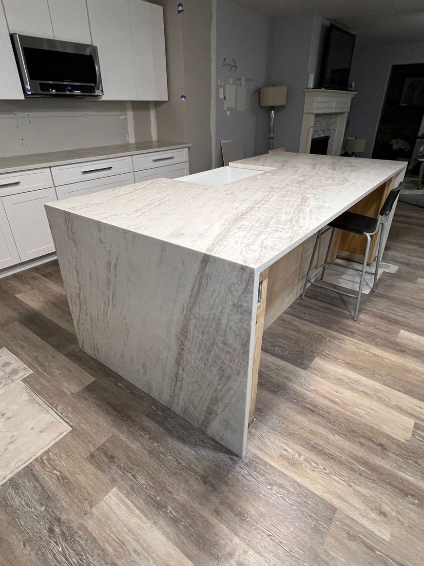 Large marble-topped kitchen island in a modern kitchen with white cabinets and wood flooring