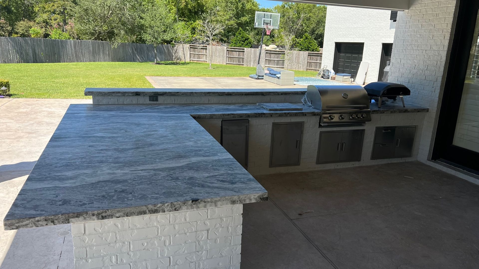 Outdoor kitchen with granite countertops, grill, and storage cabinets on a patio.
