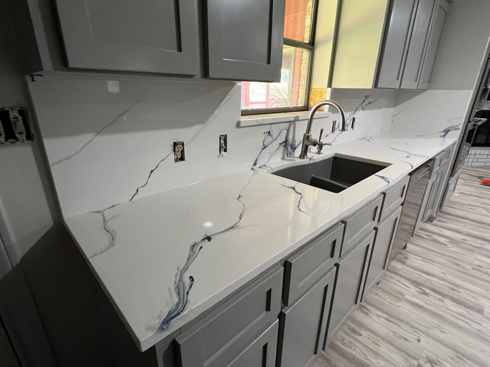 Damaged kitchen with cracked countertop, sink, gray cabinets, and light wood flooring