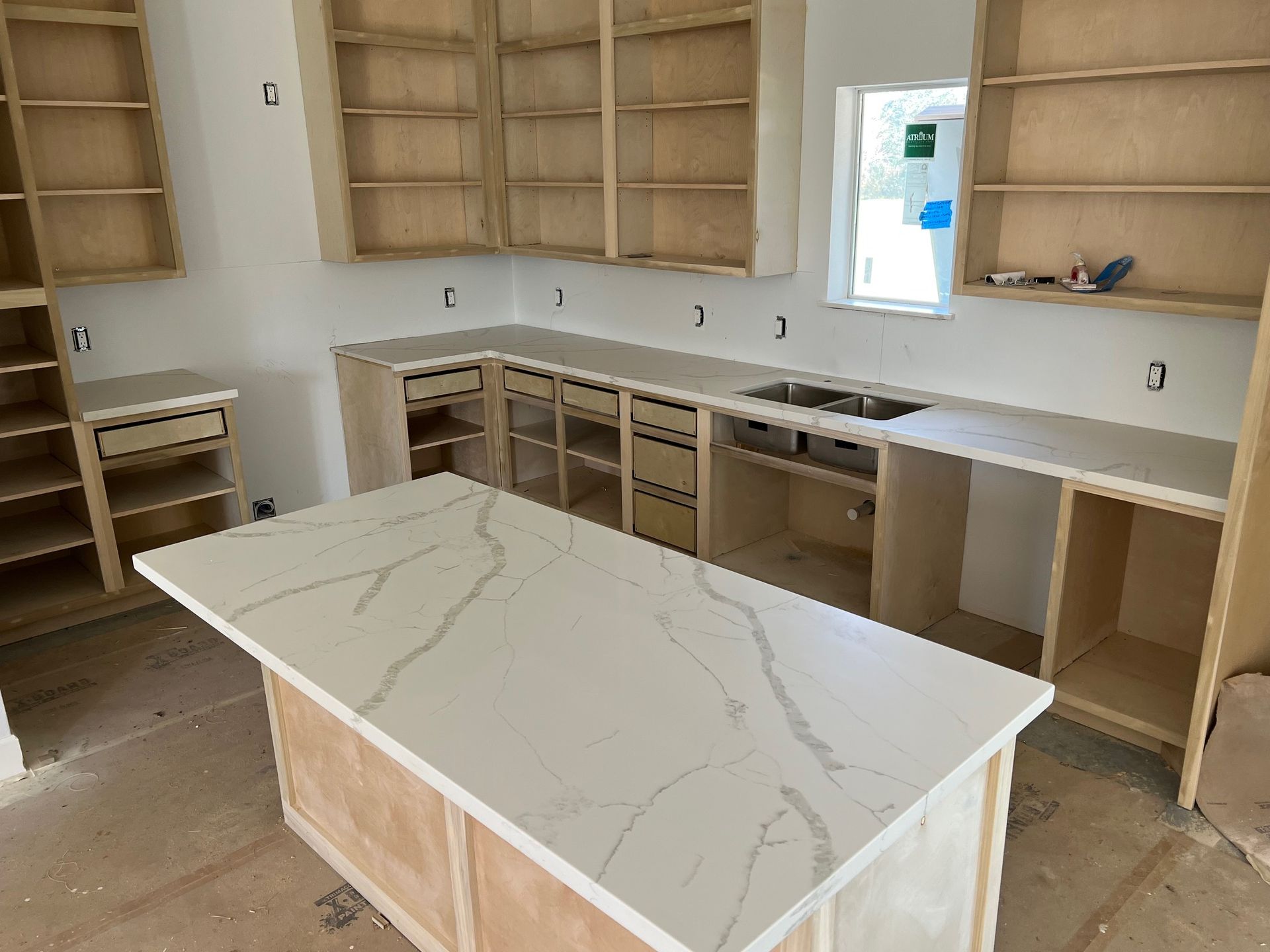 Unfinished kitchen with white cabinets, wood shelves, and a marble-look island countertop.
