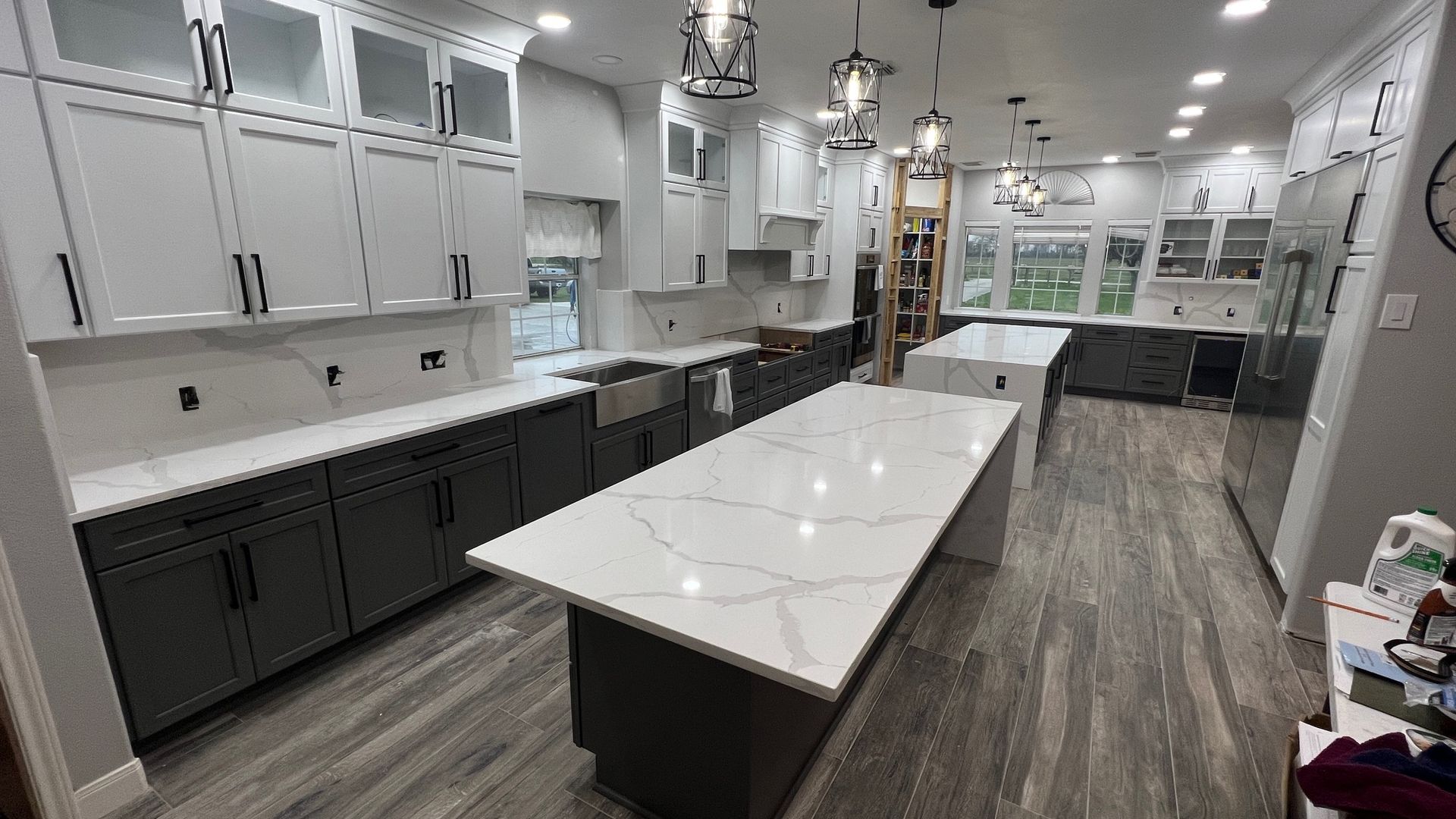Modern kitchen with gray and white cabinets, large island with a marble countertop, and wood-look flooring.