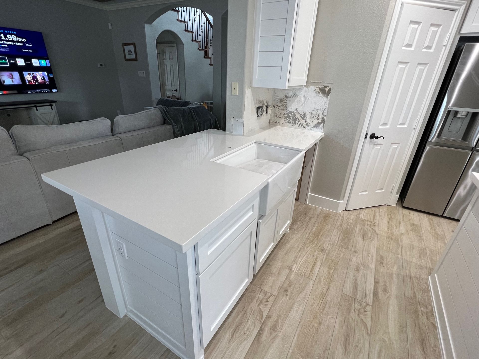 Bright kitchen with white island, light wood floors, gray sofa, and arched doorway to living room.