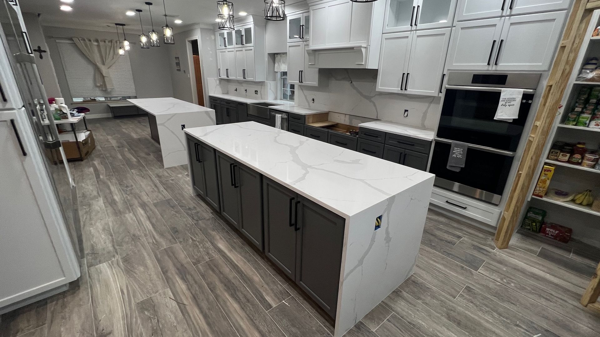 Modern kitchen with white cabinets, large island, and gray wood-look flooring