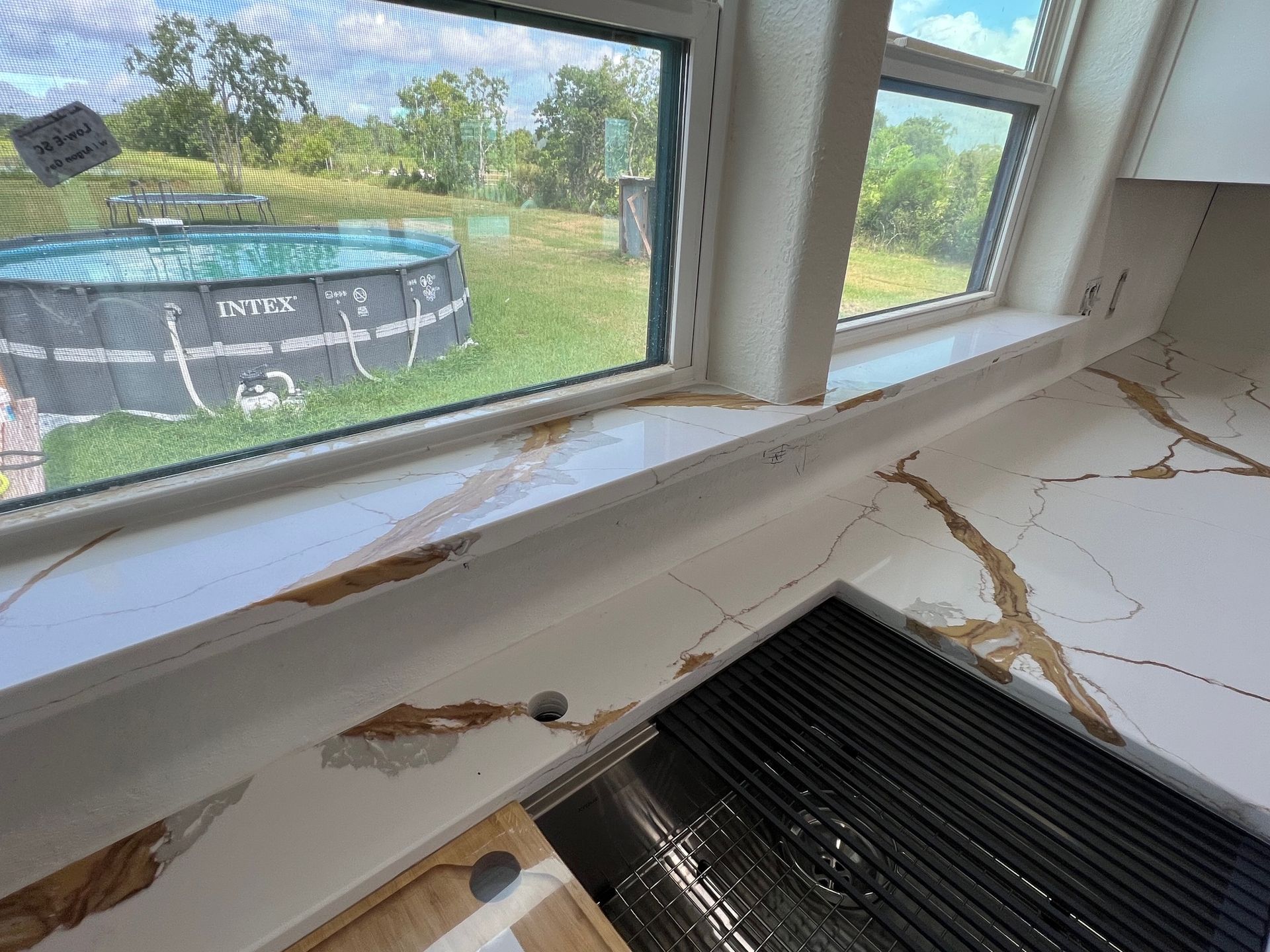 A kitchen with a view of a pool through a window.