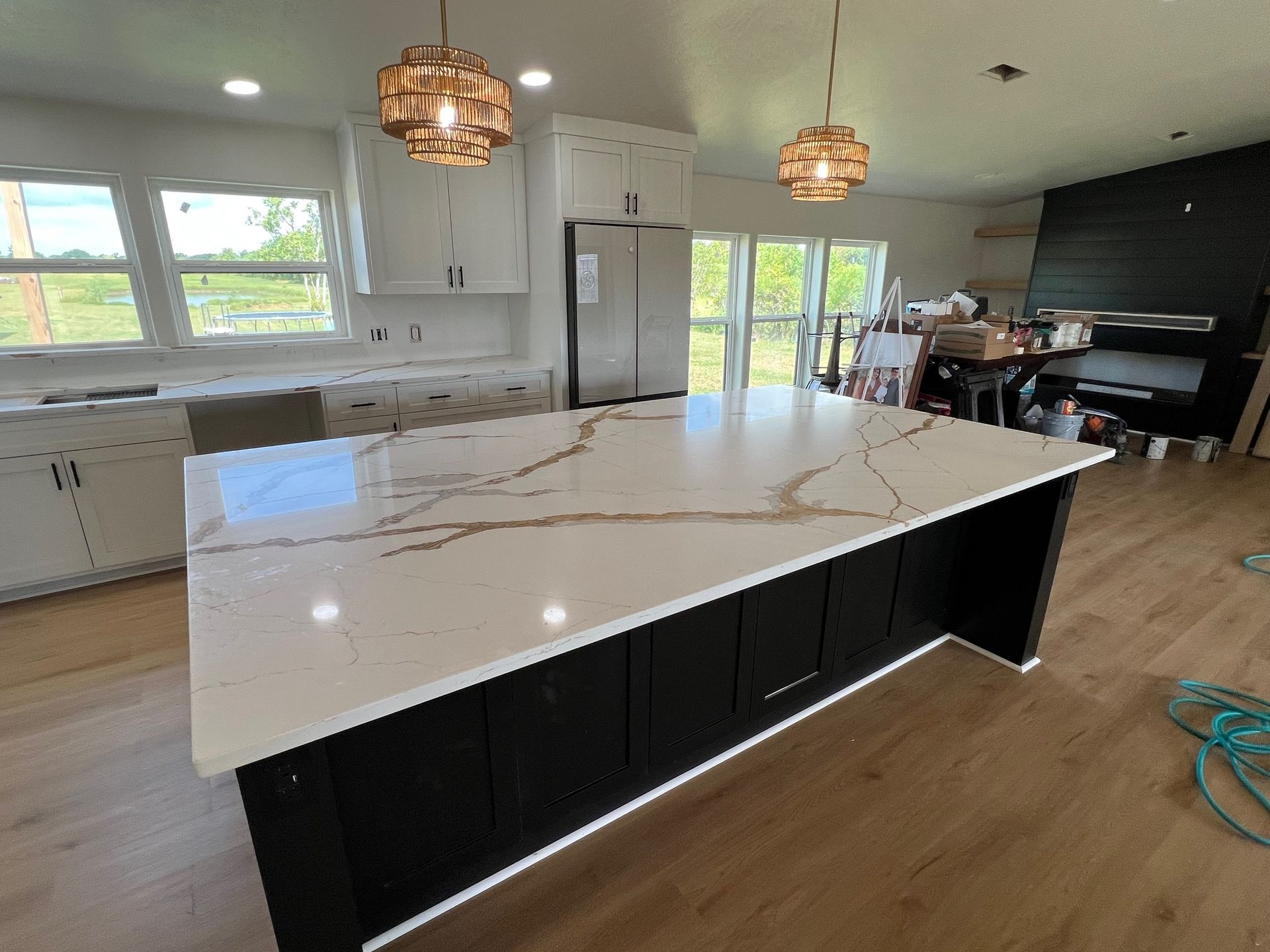 Kitchen with large island, black cabinets, white countertop with gold veining, two pendant lights.