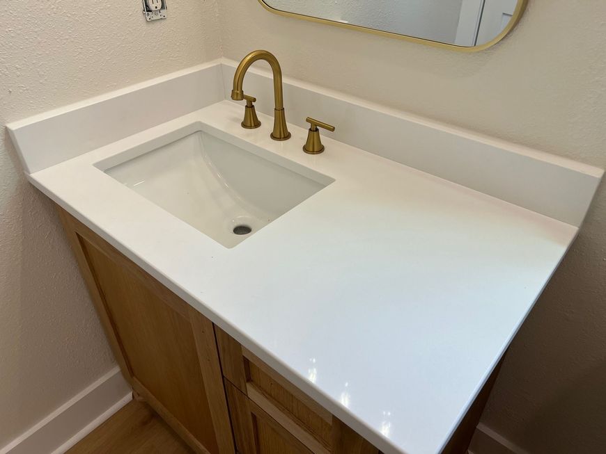 Modern bathroom vanity with white countertop, undermount sink, brass faucet, and wood cabinet underneath