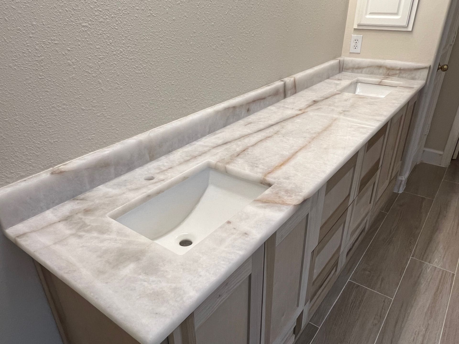 A double bathroom vanity with a white marbled countertop and white undermount sinks over light gray cabinets.