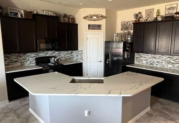 Modern kitchen with dark cabinets, white island, stainless appliances, and mosaic backsplash