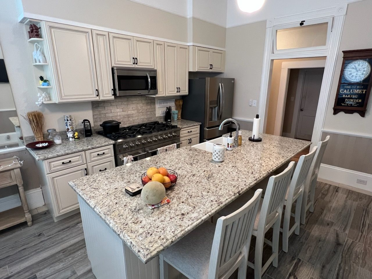 A kitchen with white cabinets, speckled granite countertops, a large center island 