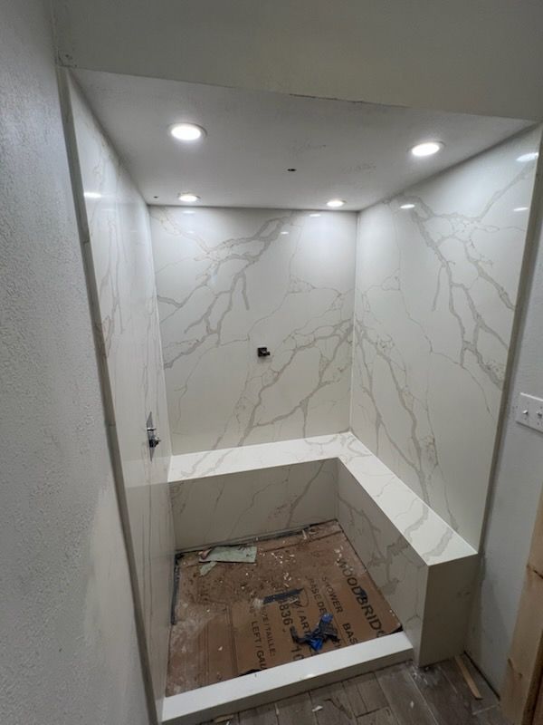 Modern, accessible shower with marble-look walls, a built-in bench, and a rain shower head.