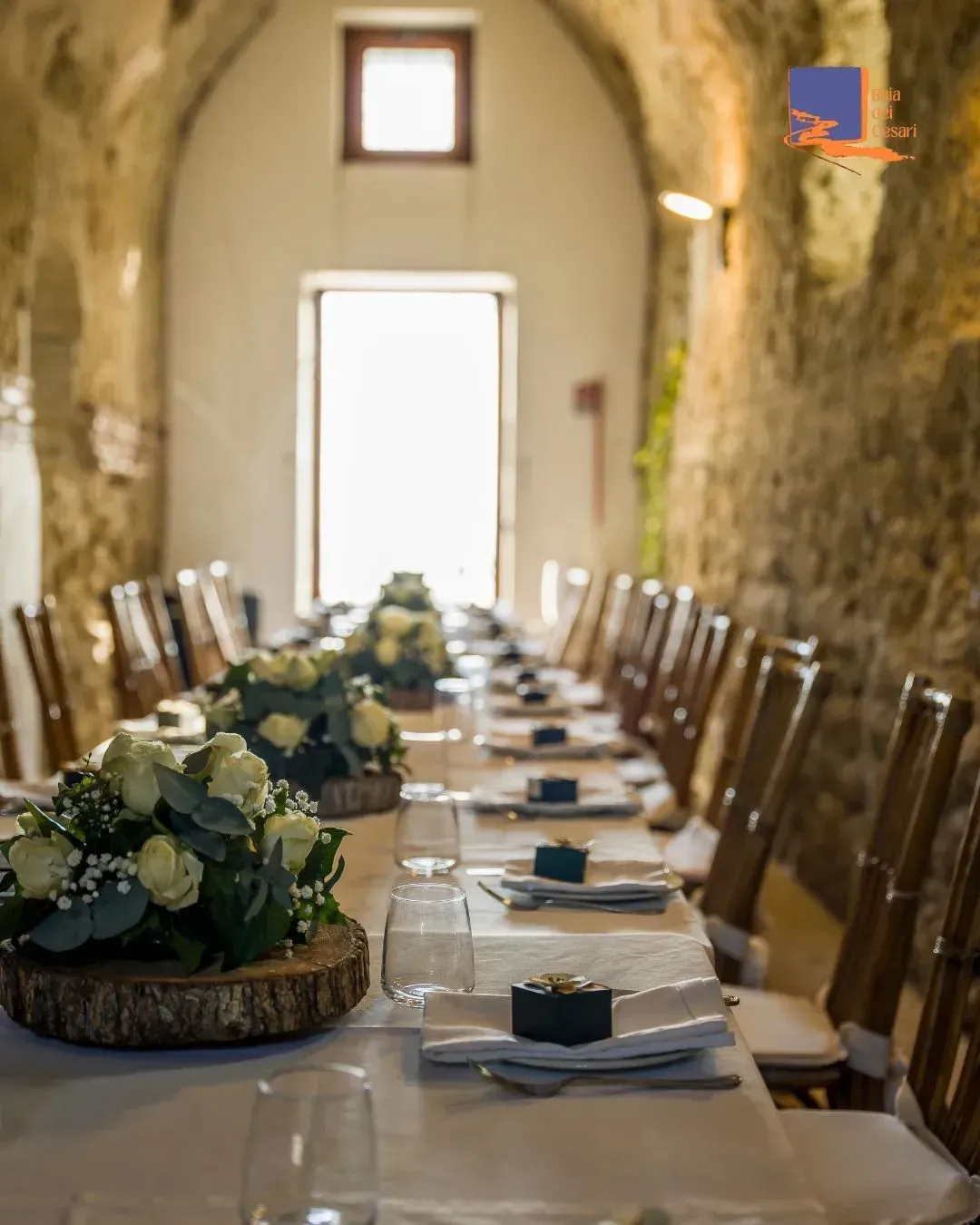 Lungo tavolo da pranzo apparecchiato per un evento formale in una stanza con pareti in pietra