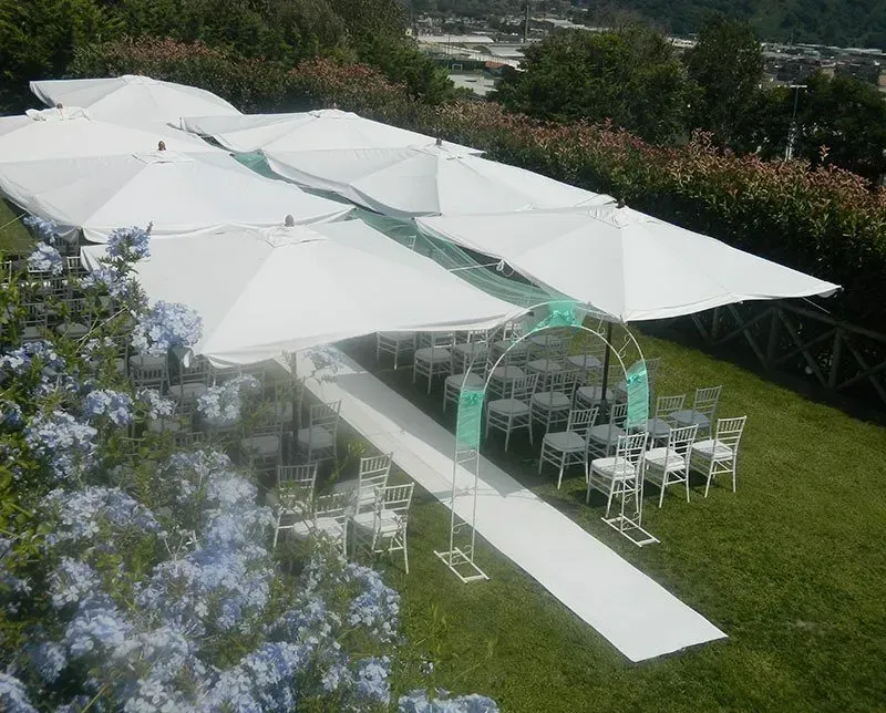 Allestimento per matrimonio all'aperto con ombrelloni bianchi, sedie e una navata su un prato verde.