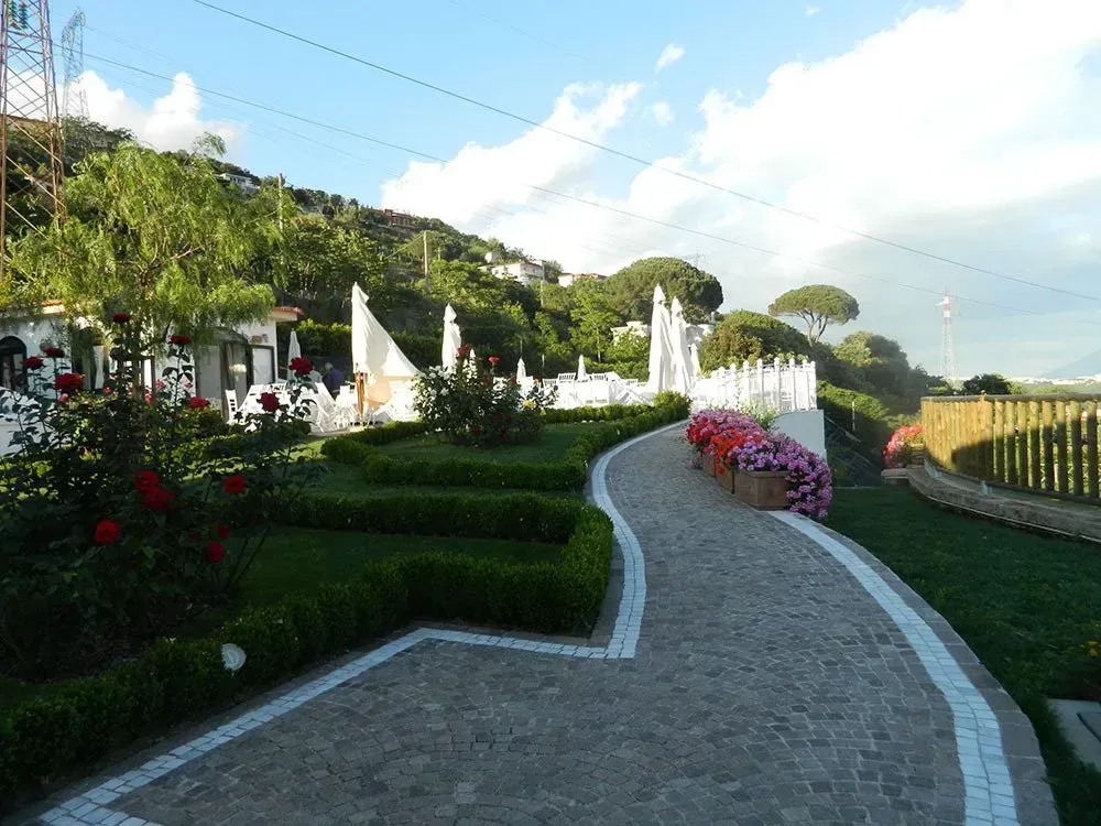 Un sentiero in pietra attraversa un giardino ben curato con fiori, siepi e strutture bianche, forse un ristorante.