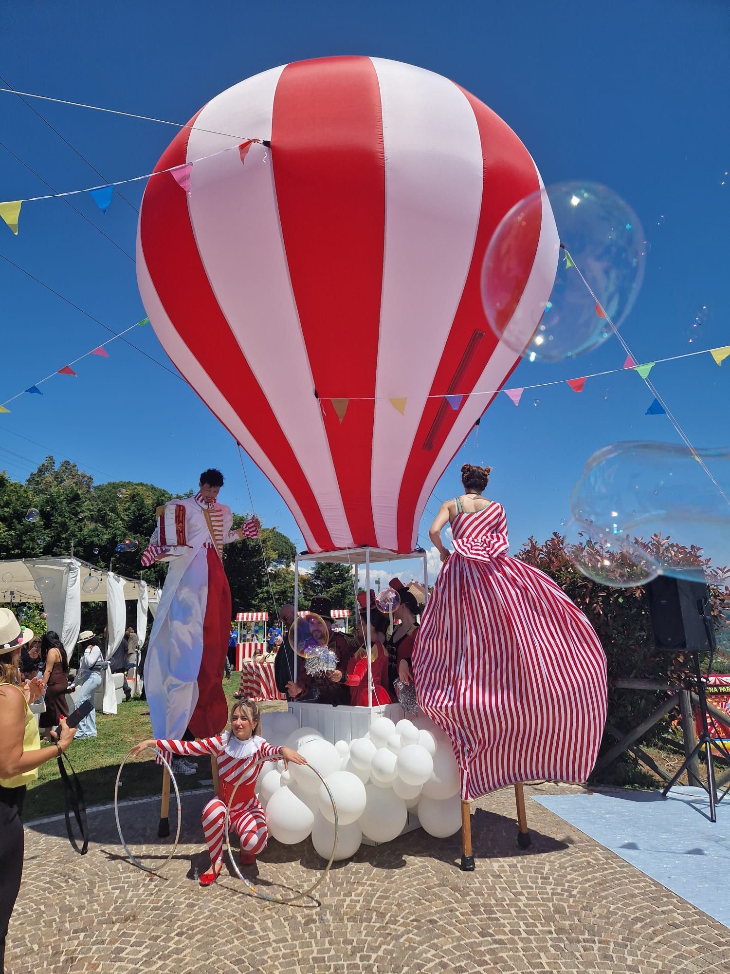 Persone in costumi a strisce su trampoli con mongolfiera