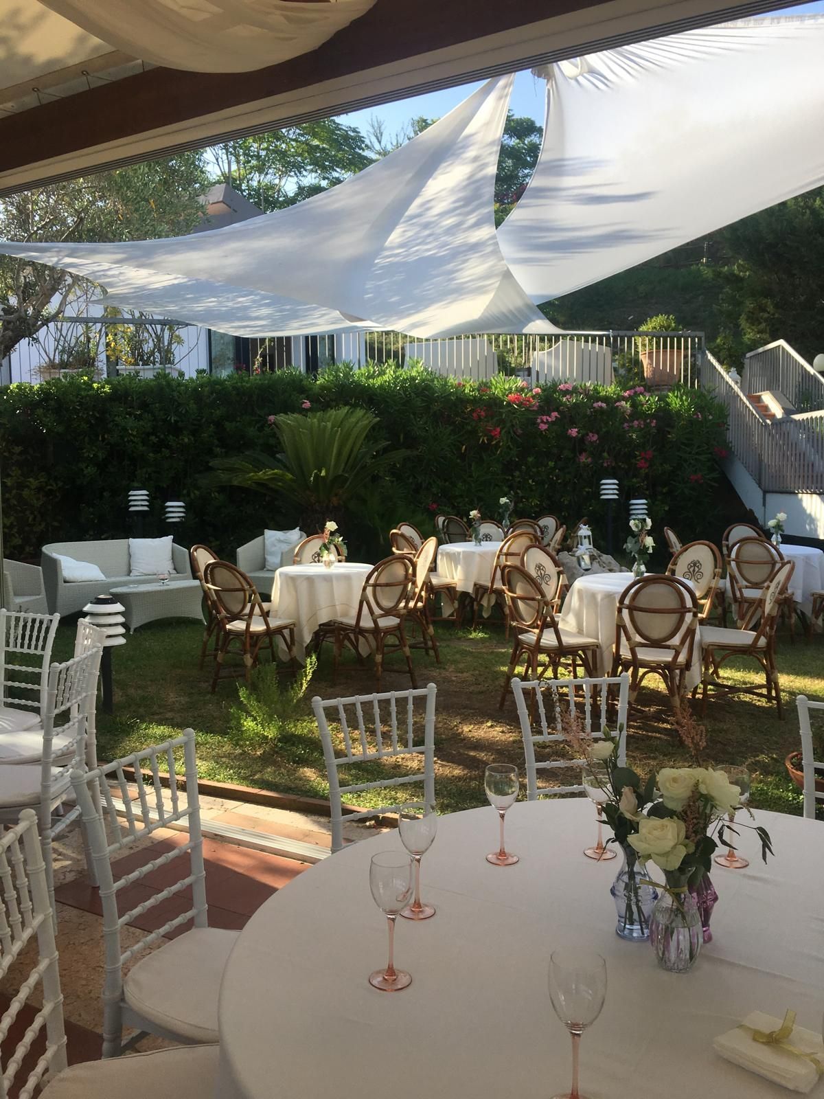 Allestimento per eventi all'aperto con tavoli, sedie e tenda in tessuto bianco.