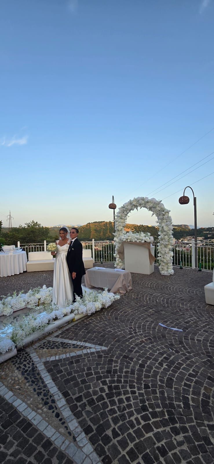 Gli sposi sono in piedi su un patio acciottolato sotto un arco ricoperto di fiori e celebrano il loro matrimonio 
