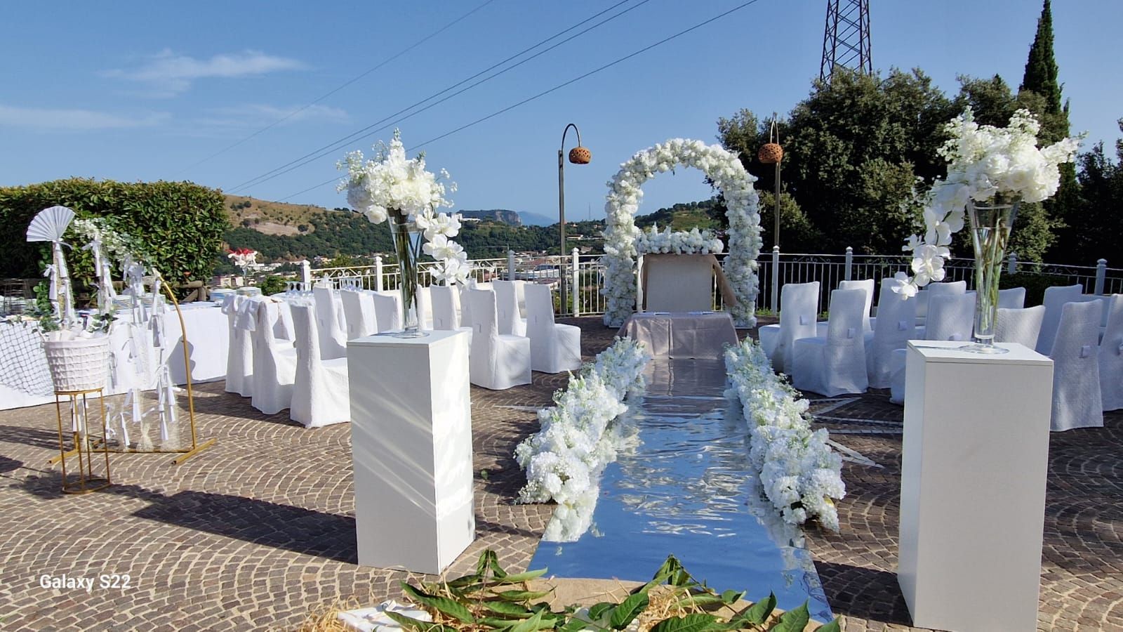 Cerimonia nuziale all'aperto con composizioni floreali bianche e runner lungo la navata.