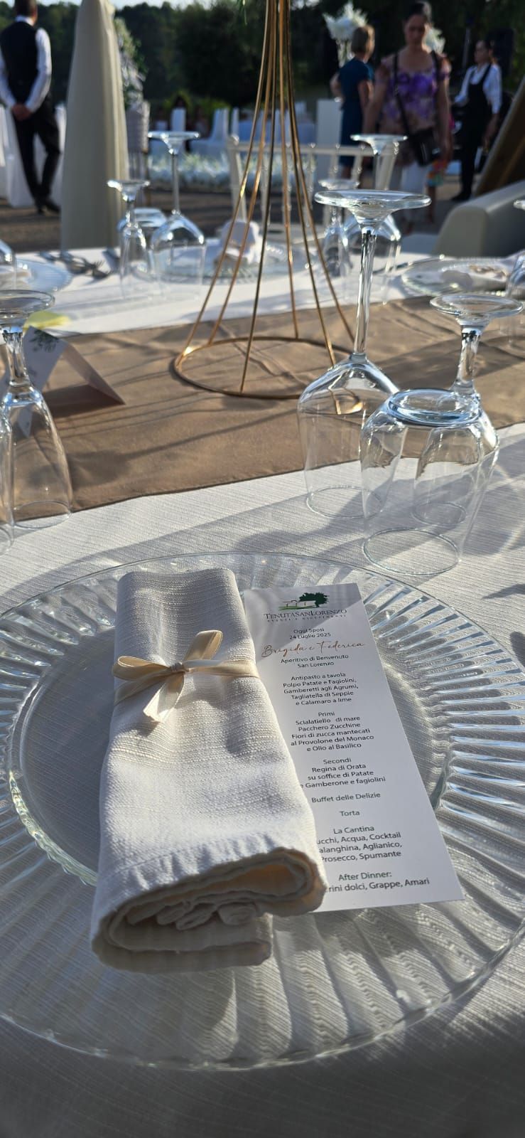 Apparecchiatura del tavolo nuziale con tovagliolo arrotolato, menù e sottopiatto in vetro trasparente.