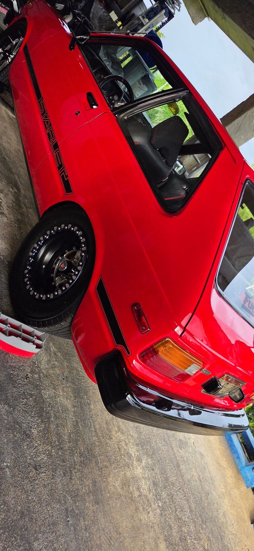 Red car with black wheels parked outside.