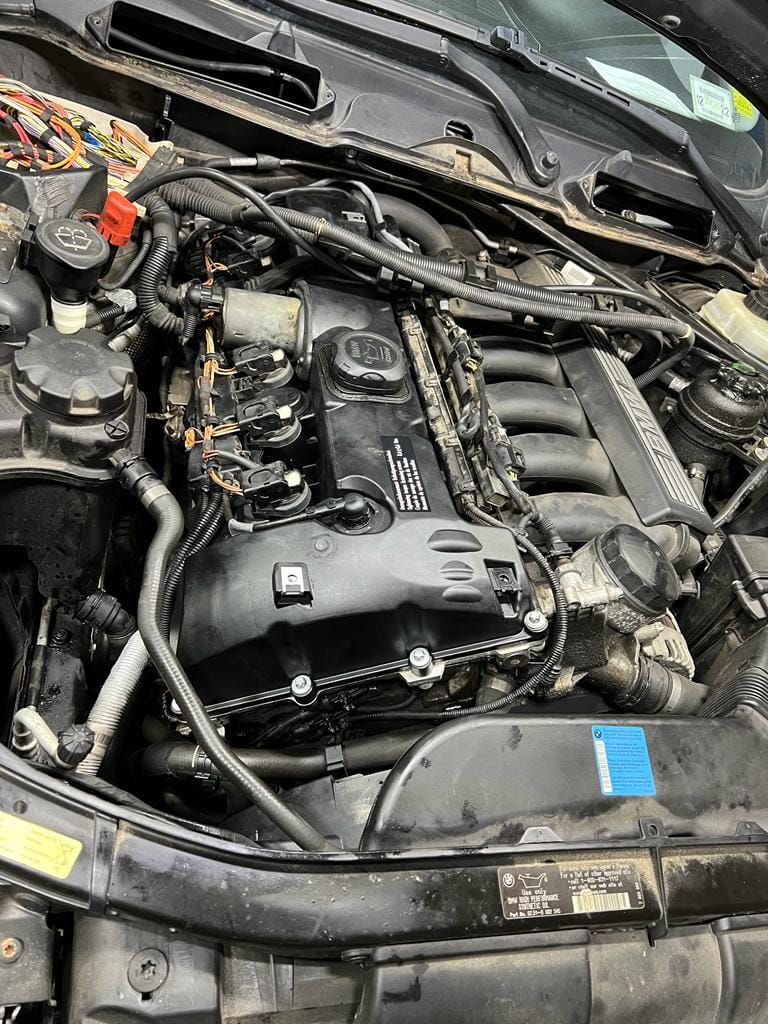 Car engine bay with black engine cover and various components.