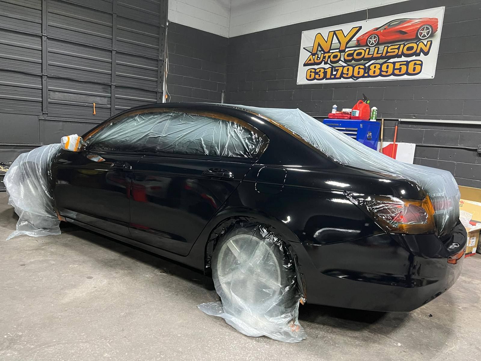 Black car in a garage, covered in plastic for painting. 
