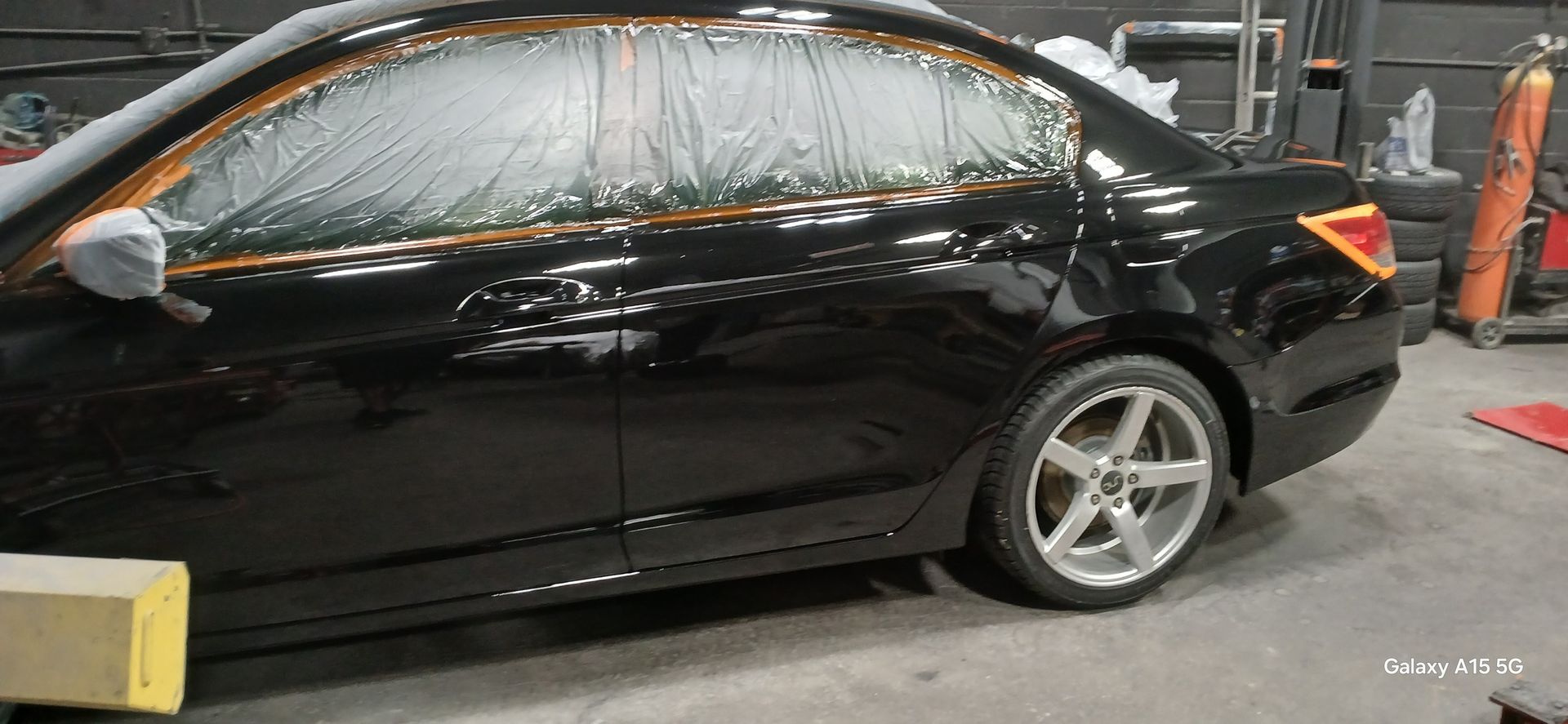 Black car in a garage, taped and covered for painting.