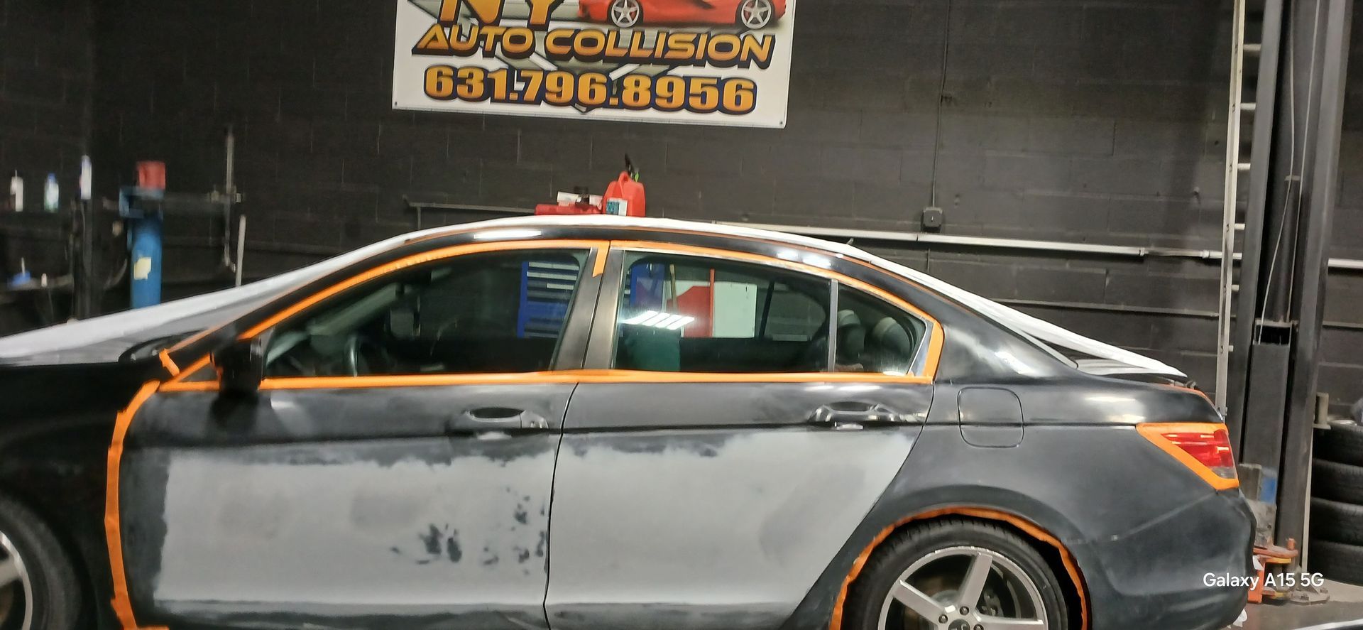 Car being repaired in an auto collision shop. Masking tape around windows and body panels, indicating repair and painting.