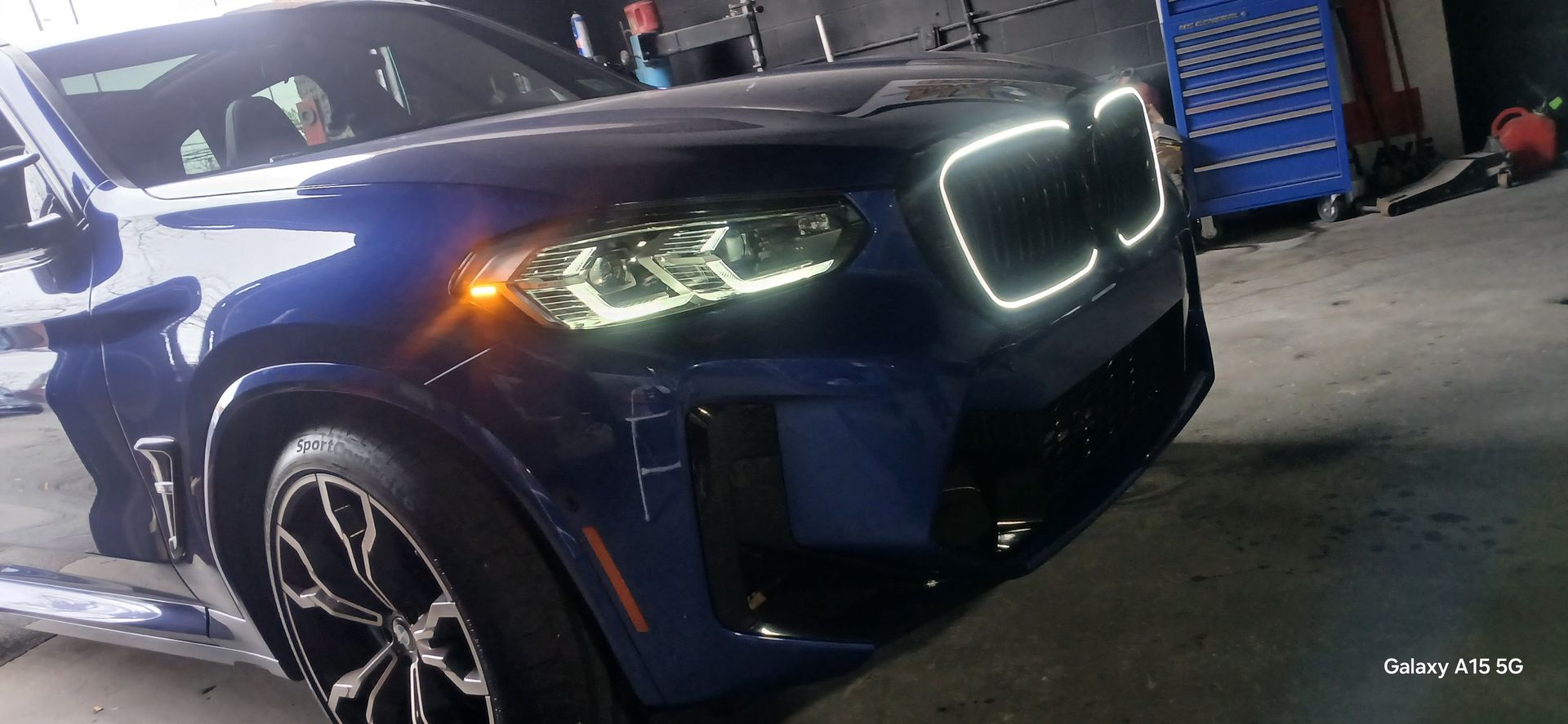 A blue BMW SUV with glowing headlights and grille in a garage.