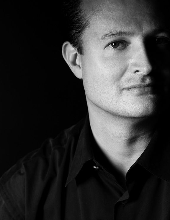 A man in a black shirt is looking at the camera in a black and white photo.