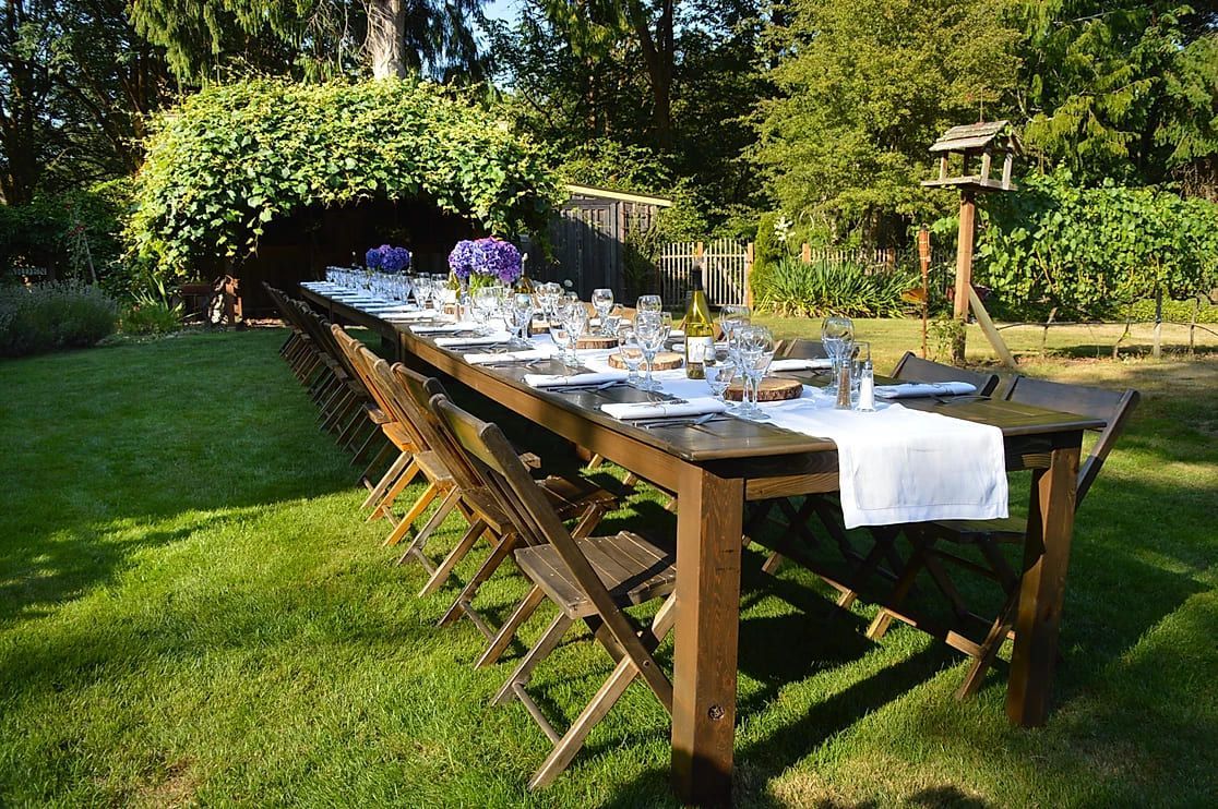A long wooden table and chairs are sitting on top of a lush green field.