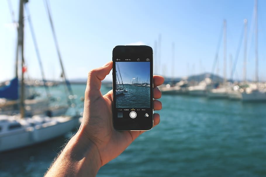A person is holding a cell phone in their hand and taking a picture of boats in the water.