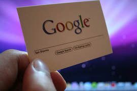 A person is holding a google business card in front of a computer screen.