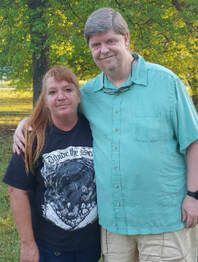 A man and a woman are posing for a picture in a park.