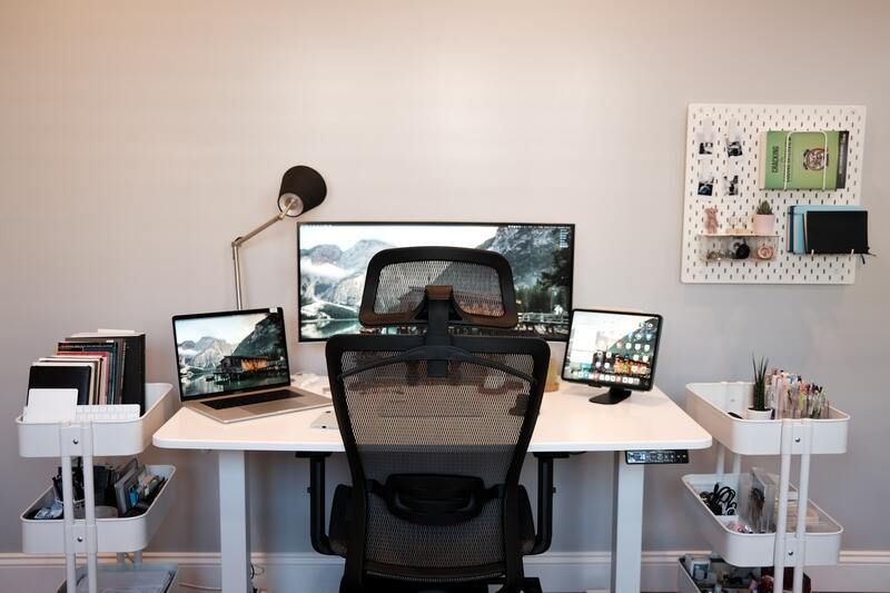 A desk with two monitors , a laptop , and a chair.