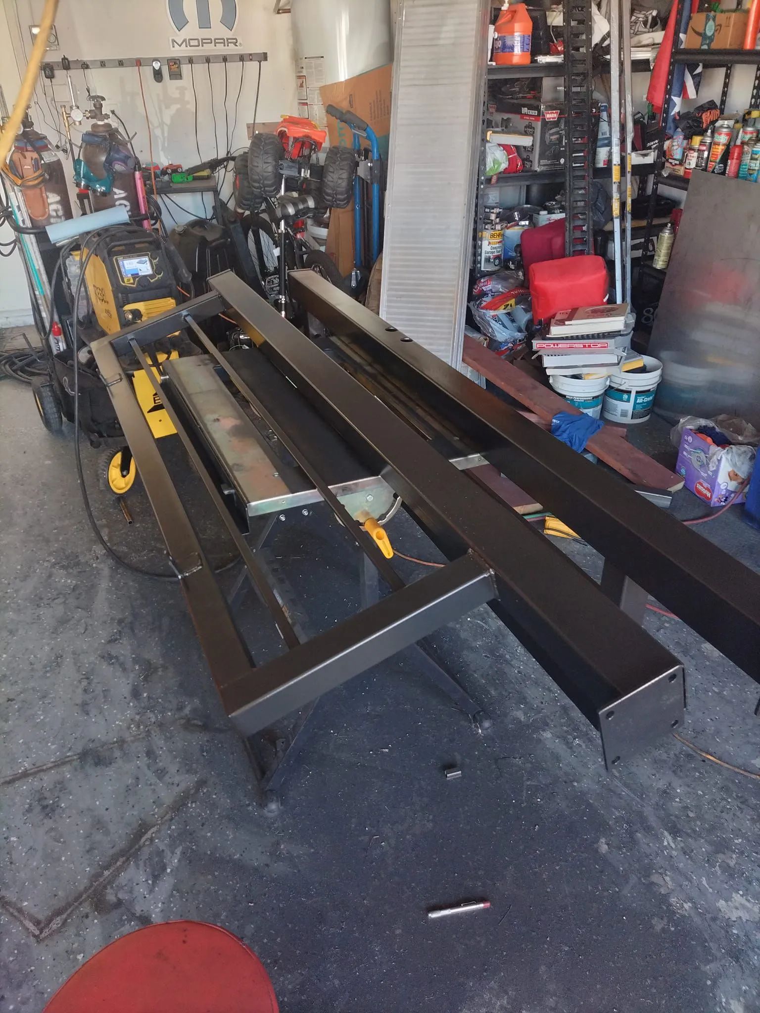 Black metal frame structures on a garage floor with tools and equipment in the background.