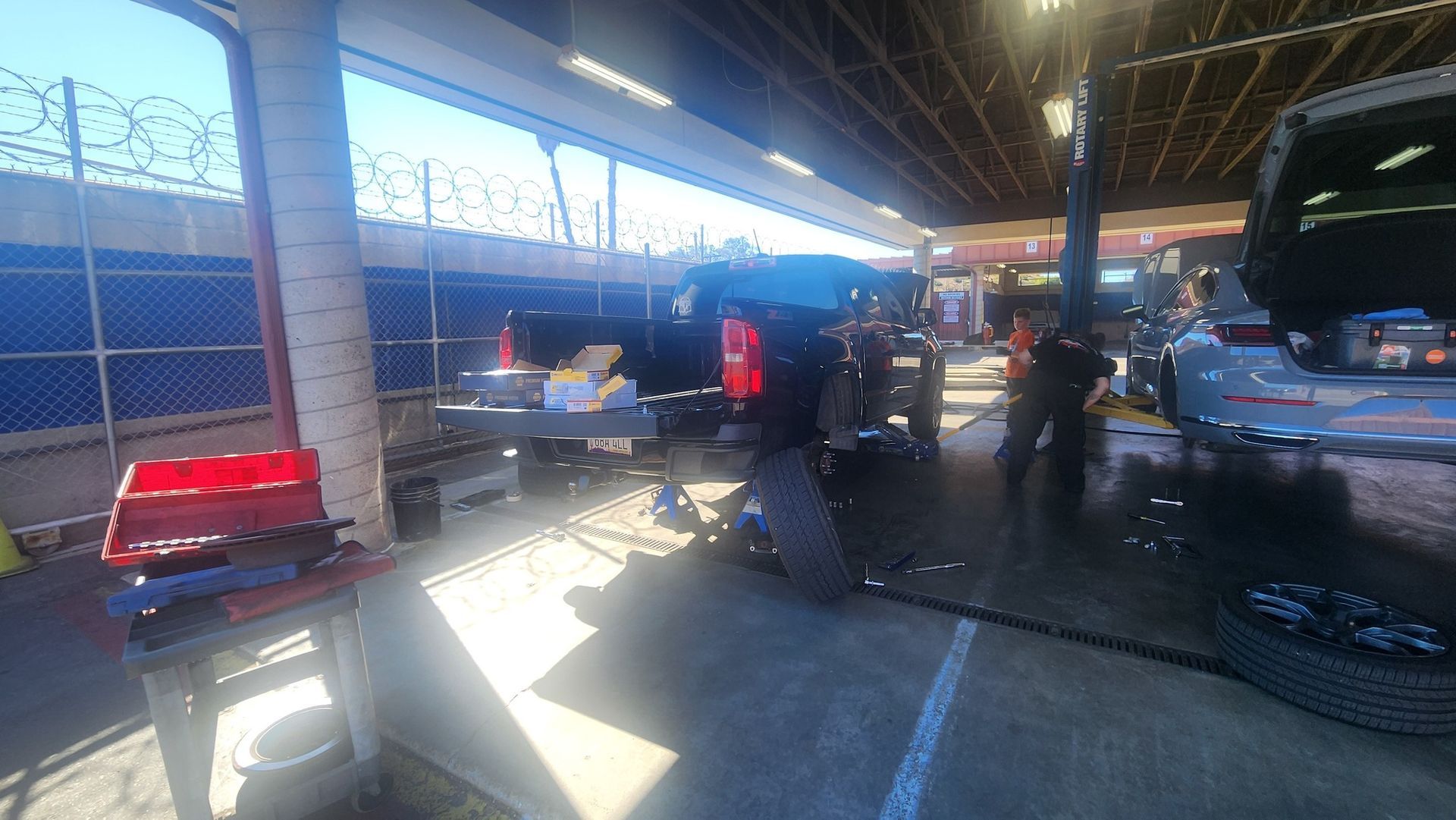 A car repair shop with a car on a lift. Mechanics work on a vehicle, tools visible.