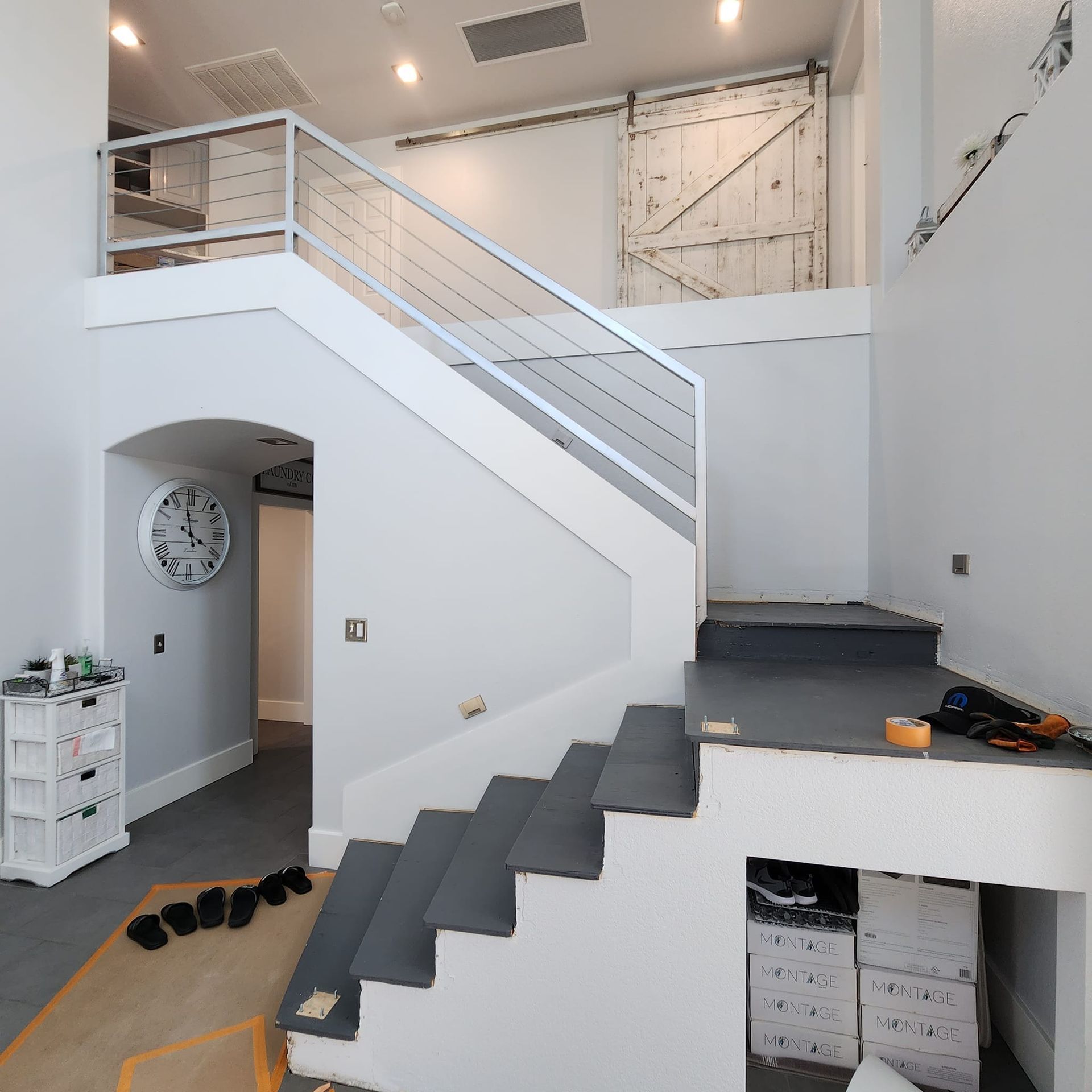 A modern interior with stairs leading to a loft. Gray steps, white walls, and a large clock.