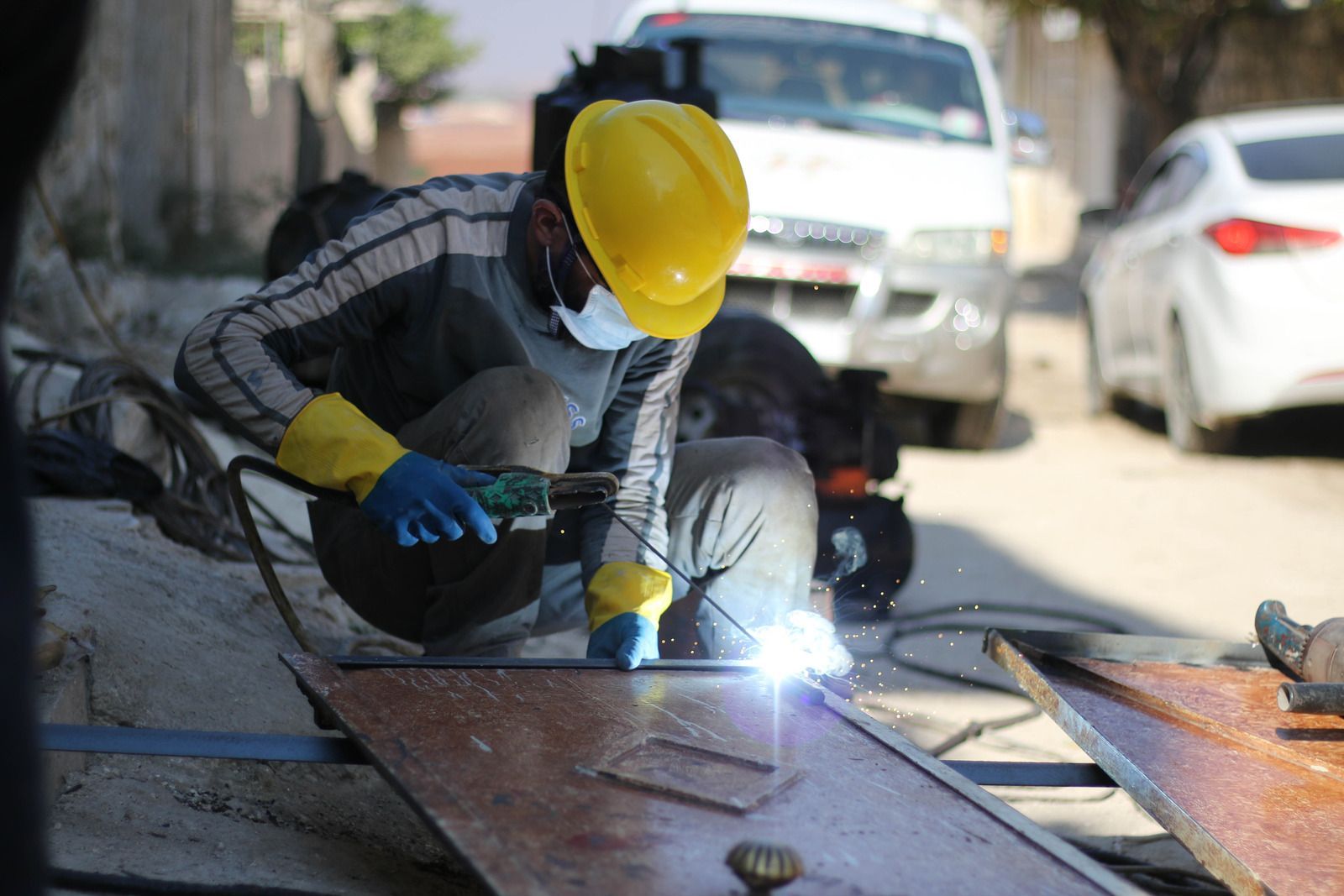Welder in yellow helmet and mask, welding metal outdoors.