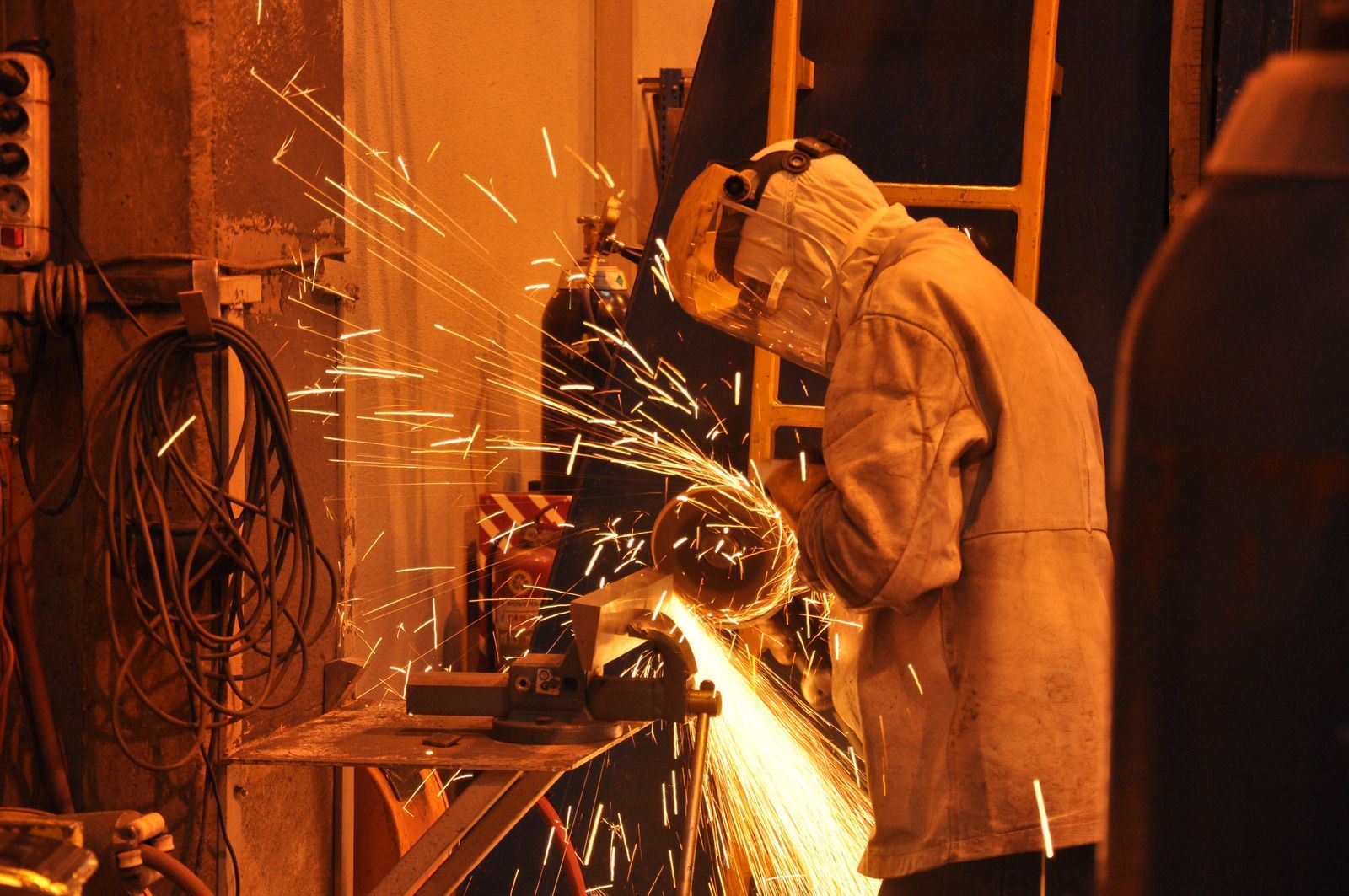 A worker in protective gear using a grinder, creating sparks in a workshop.