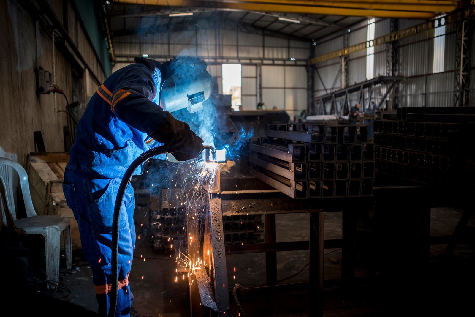 Welder in blue work suit welding metal in a workshop, sparks flying.