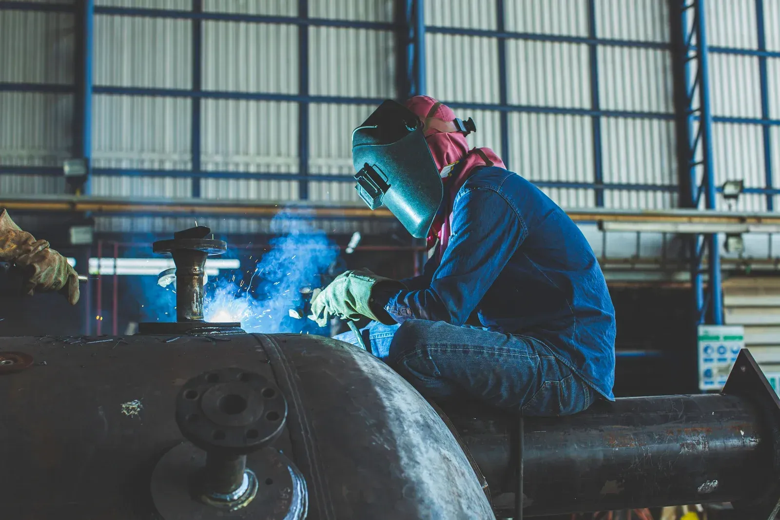 A man is welding a piece of metal in a factory.