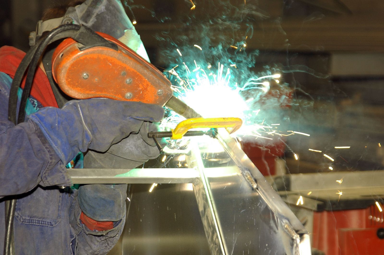 A man is welding a piece of metal in a factory