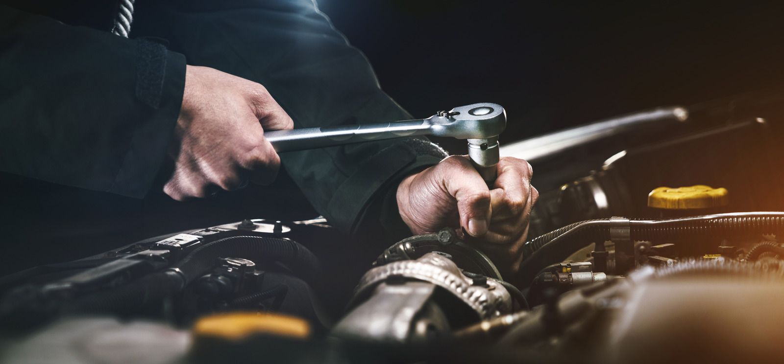 A man is working on a car engine with a wrench.