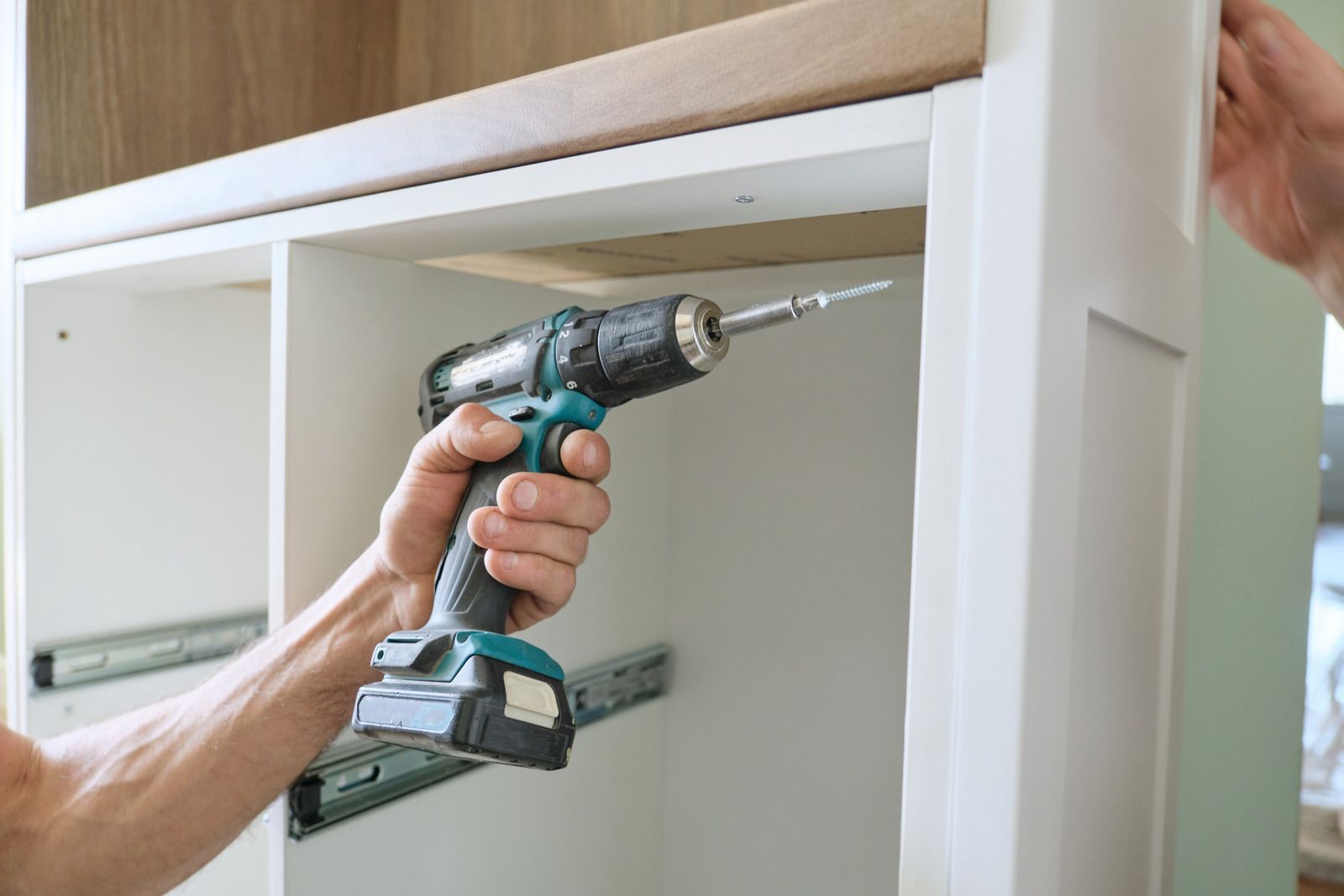 A man is using a cordless drill to install a cabinet.